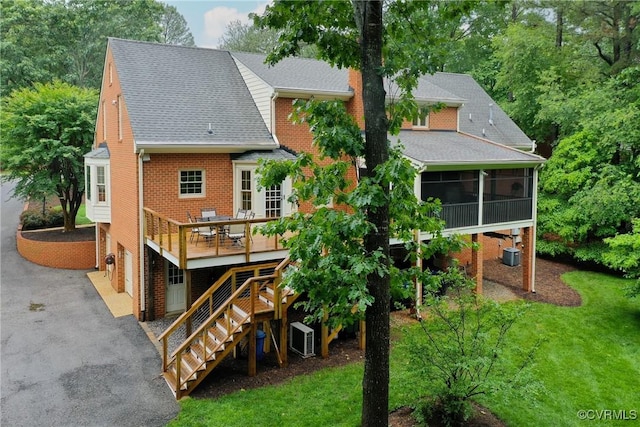 rear view of property with a sunroom, a wooden deck, stairs, driveway, and roof with shingles