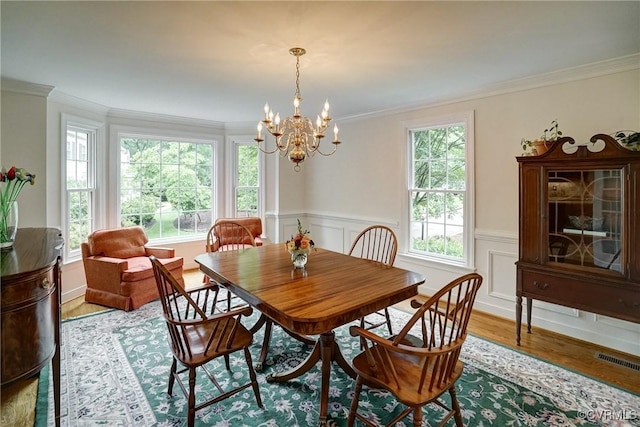 dining space with wood finished floors, crown molding, a chandelier, and wainscoting