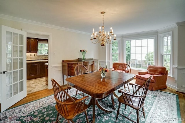 dining area featuring crown molding, a chandelier, light wood finished floors, a wainscoted wall, and a decorative wall
