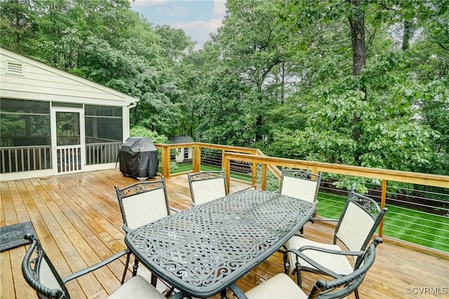 wooden terrace featuring outdoor dining space, a sunroom, a grill, and view of wooded area
