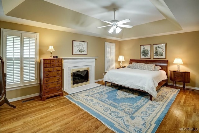 bedroom featuring a raised ceiling, baseboards, wood finished floors, and a glass covered fireplace