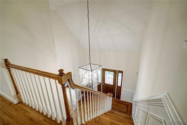 stairway featuring a chandelier, wood finished floors, a decorative wall, and wainscoting