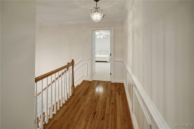 hallway with an upstairs landing, crown molding, wood finished floors, a chandelier, and a decorative wall