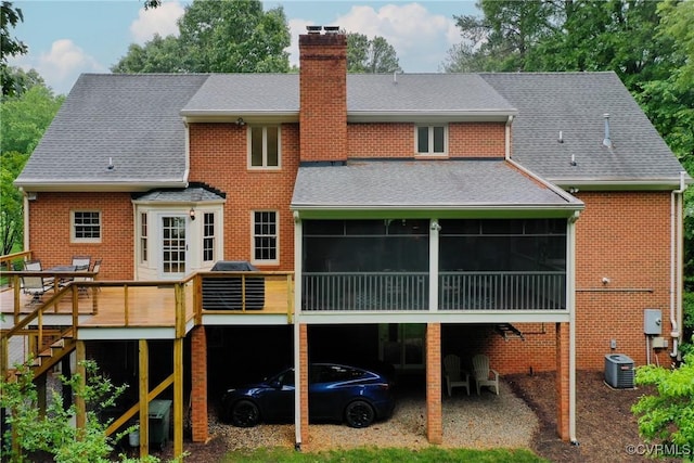 rear view of house featuring a chimney, a sunroom, a deck, a shingled roof, and brick siding