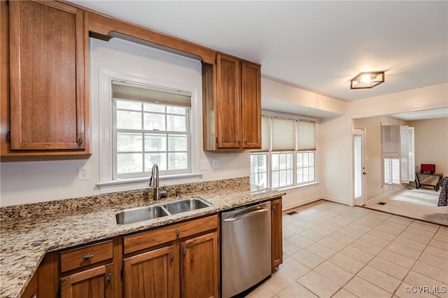 kitchen featuring stainless steel dishwasher, a sink, brown cabinetry, light tile patterned flooring, and light stone countertops
