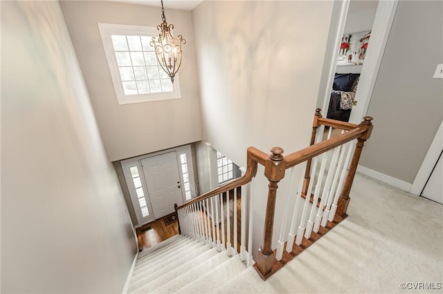 stairs with a chandelier, healthy amount of natural light, baseboards, and carpet floors