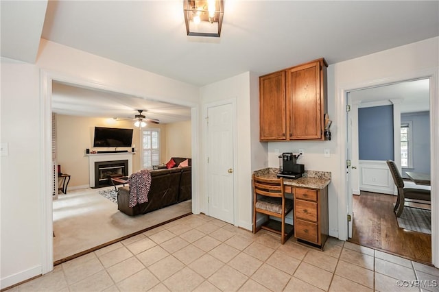 kitchen featuring brown cabinetry, a ceiling fan, light tile patterned flooring, a glass covered fireplace, and open floor plan
