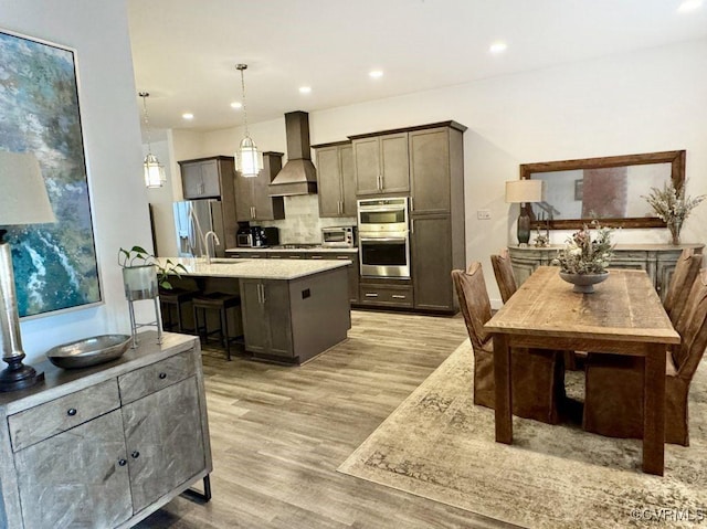 5112 Old Main St, Henrico, VA 23231 - kitchen featuring wall chimney range hood, appliances with stainless steel finishes, decorative backsplash, a breakfast bar, and light wood-style floors