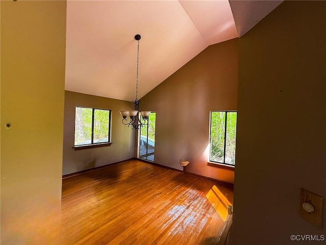 spare room featuring wood finished floors, a chandelier, high vaulted ceiling, and baseboards