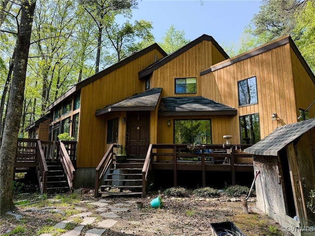 view of front of home with a wooden deck, stairs, and roof with shingles