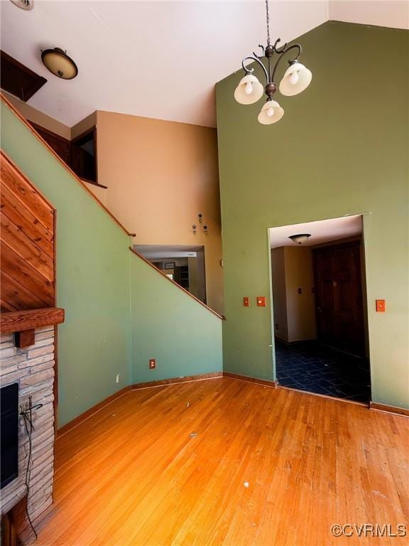 unfurnished living room with a towering ceiling, wood finished floors, a chandelier, a fireplace, and stairs