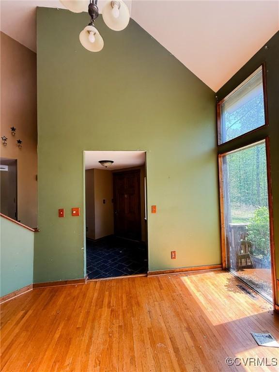 empty room featuring high vaulted ceiling, wood finished floors, and baseboards