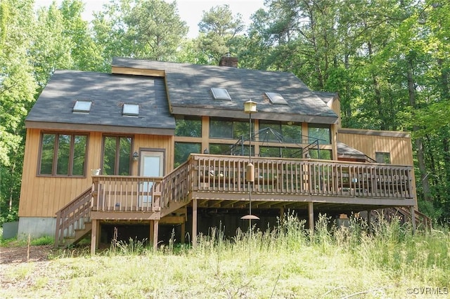 rear view of property featuring a deck, stairs, a chimney, and a shingled roof