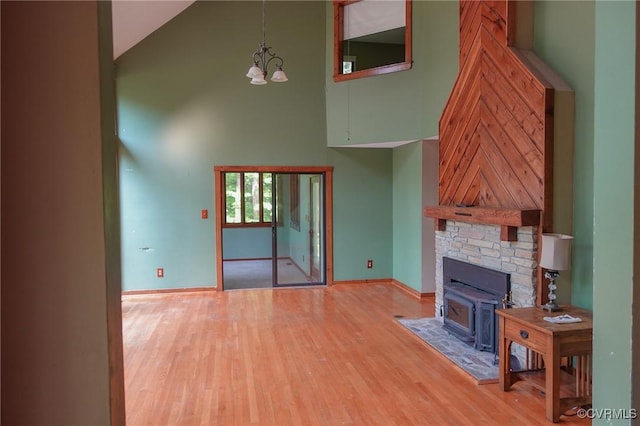 unfurnished living room with high vaulted ceiling, light wood finished floors, baseboards, a chandelier, and a wood stove