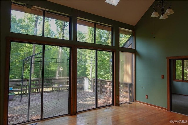 doorway featuring high vaulted ceiling, wood finished floors, plenty of natural light, baseboards, and a skylight