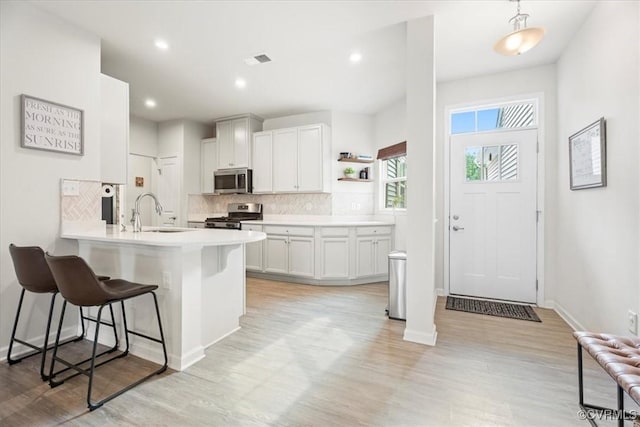 kitchen with appliances with stainless steel finishes, a sink, a breakfast bar area, light wood-type flooring, and decorative backsplash