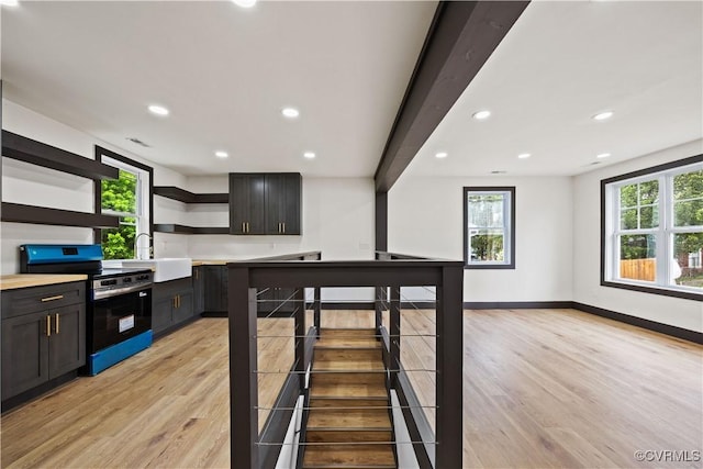 kitchen featuring stainless steel electric stove, open shelves, a sink, light wood-type flooring, and light countertops