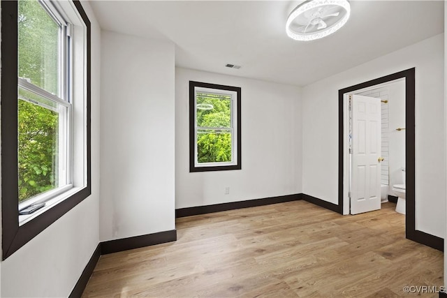 spare room featuring plenty of natural light, baseboards, and light wood-type flooring