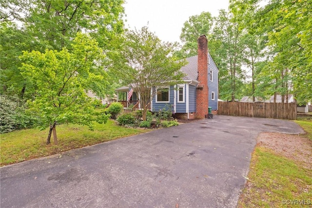 view of front facade with a chimney, driveway, and fence