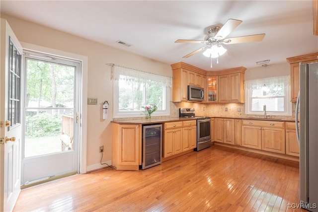 kitchen with stainless steel appliances, beverage cooler, light wood-style flooring, a sink, and plenty of natural light