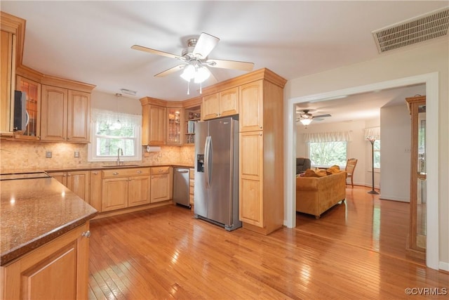 kitchen featuring stainless steel appliances, a ceiling fan, a sink, tasteful backsplash, and glass insert cabinets