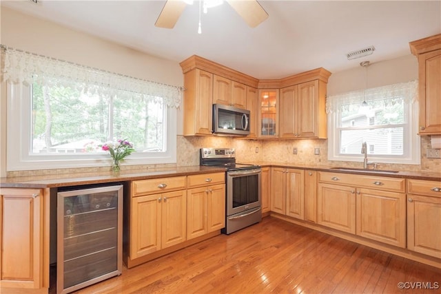 kitchen with appliances with stainless steel finishes, wine cooler, a sink, light wood-style floors, and healthy amount of natural light