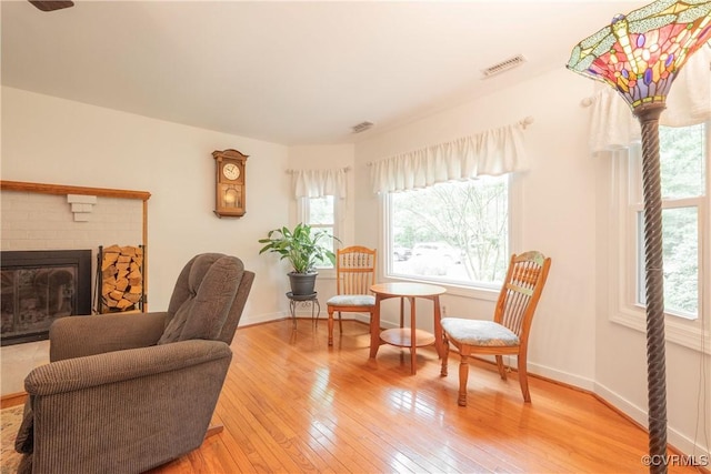 sitting room with plenty of natural light, light wood finished floors, a brick fireplace, and baseboards