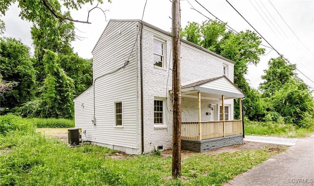 view of side of home with central AC unit, crawl space, brick siding, and covered porch