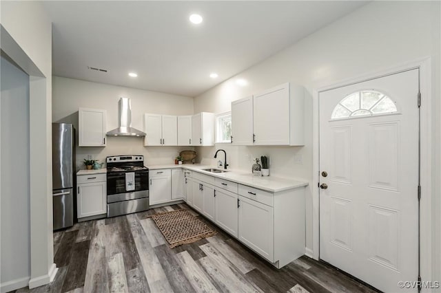 kitchen with stainless steel appliances, wall chimney range hood, a sink, white cabinetry, and healthy amount of natural light