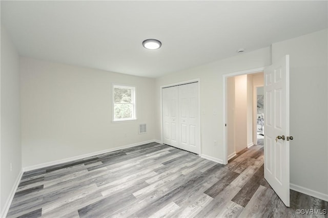 unfurnished bedroom with wood finished floors, baseboards, and a closet