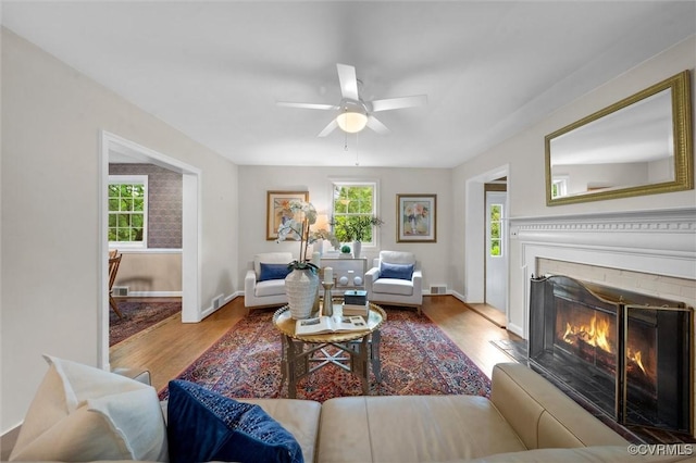 living room with wood finished floors, a ceiling fan, a lit fireplace, and baseboards