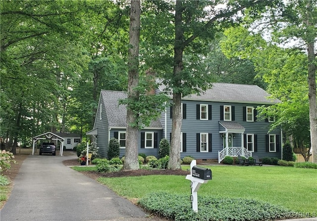 colonial home with a front yard, a shingled roof, a detached carport, and driveway