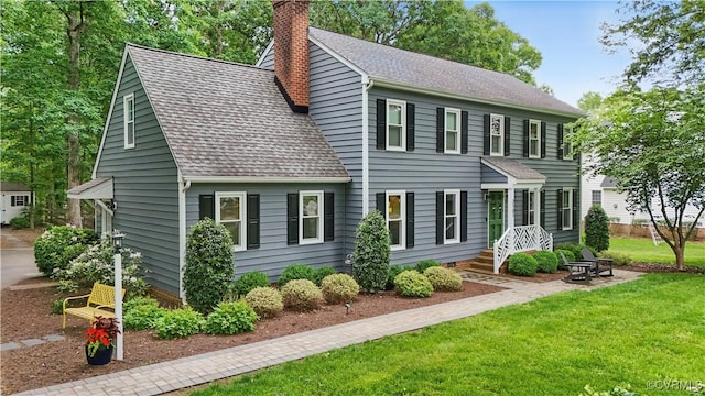 back of property featuring a chimney, roof with shingles, and a lawn