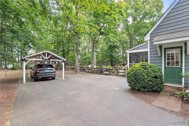 view of patio / terrace featuring a carport, a sunroom, asphalt driveway, and view of scattered trees