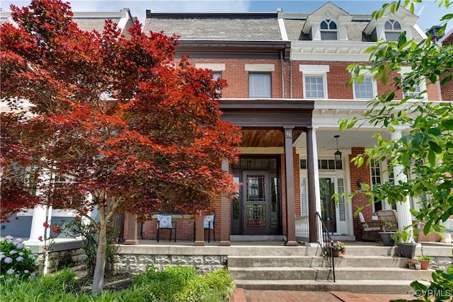 view of front of property with mansard roof, brick siding, covered porch, and a high end roof