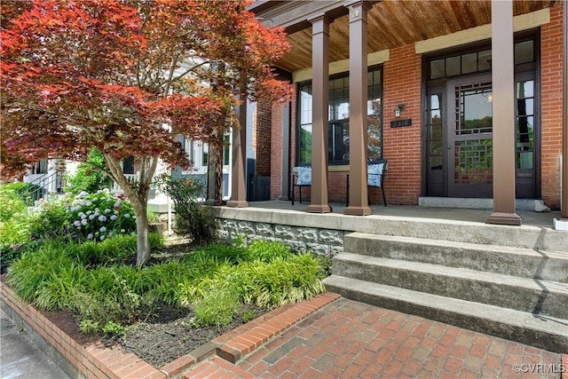 view of exterior entry featuring covered porch and brick siding
