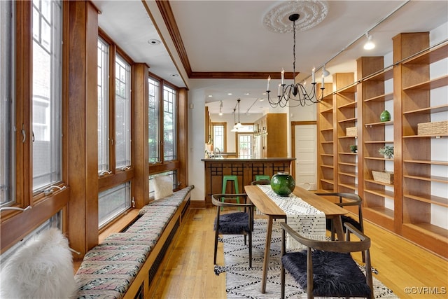 dining space with a chandelier, light wood finished floors, baseboards, rail lighting, and crown molding