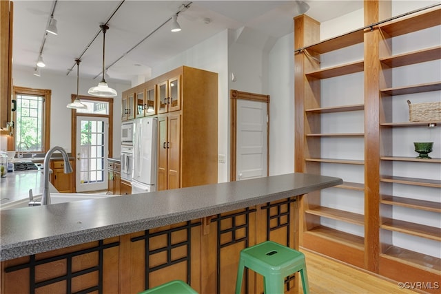 kitchen with rail lighting, white appliances, brown cabinetry, and a sink
