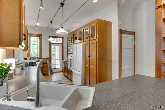 kitchen with brown cabinetry, a sink, white appliances, glass insert cabinets, and track lighting