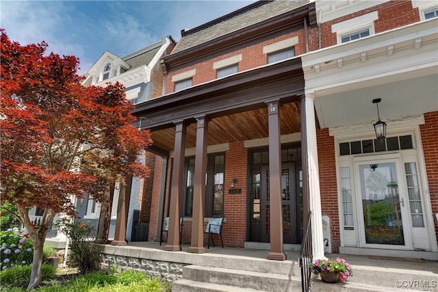 view of exterior entry featuring a porch and brick siding