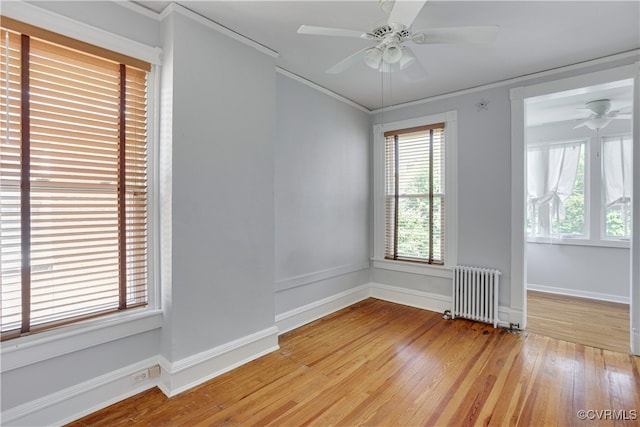 empty room featuring radiator heating unit, plenty of natural light, light wood-type flooring, and ornamental molding