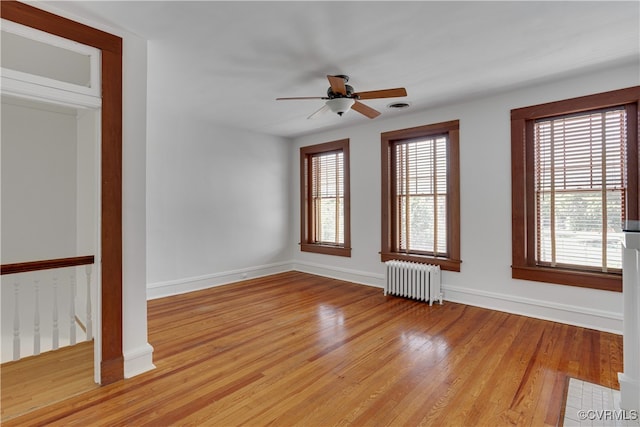 unfurnished room featuring radiator, healthy amount of natural light, ceiling fan, and light wood finished floors