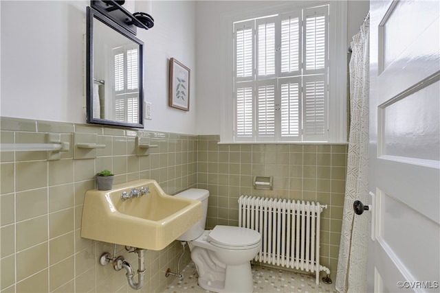 bathroom with radiator, toilet, healthy amount of natural light, tile walls, and a wainscoted wall