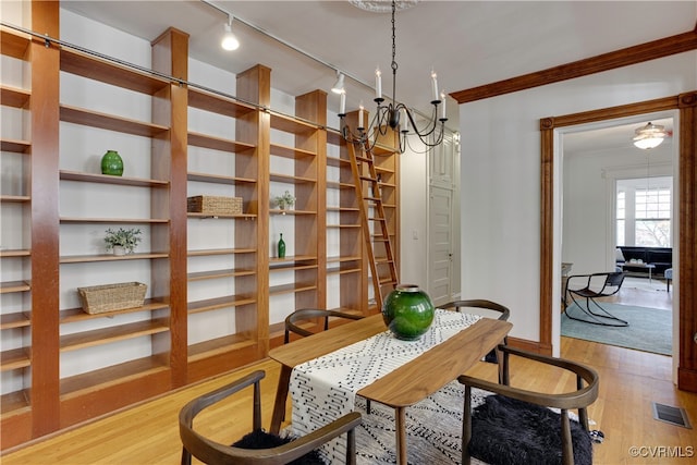 dining space with a chandelier, wood finished floors, rail lighting, crown molding, and baseboards