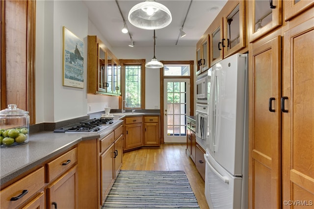 kitchen with white appliances, light wood-style flooring, rail lighting, glass insert cabinets, and a sink