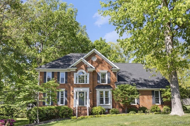colonial-style house featuring a front lawn and brick siding