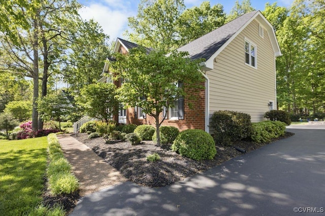 view of home's exterior featuring brick siding, a shingled roof, and a lawn