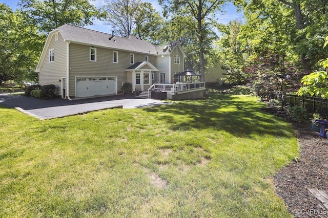 rear view of property featuring an attached garage, a deck, a lawn, and driveway