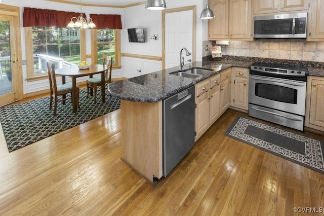 kitchen featuring appliances with stainless steel finishes, a sink, wood finished floors, a chandelier, and a peninsula