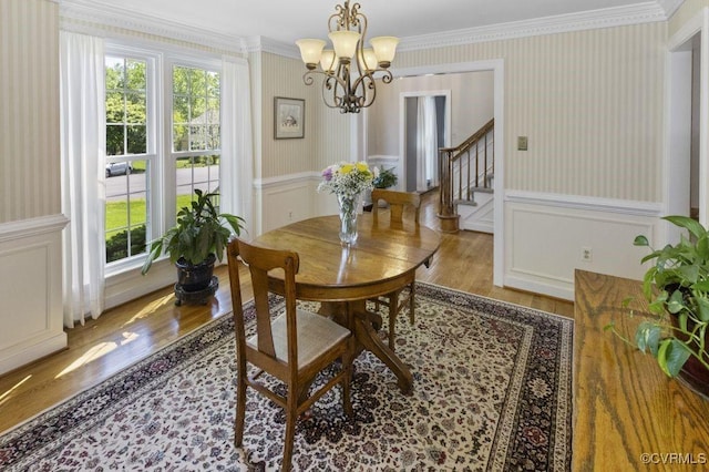 dining space featuring wood finished floors, a chandelier, wallpapered walls, crown molding, and stairway